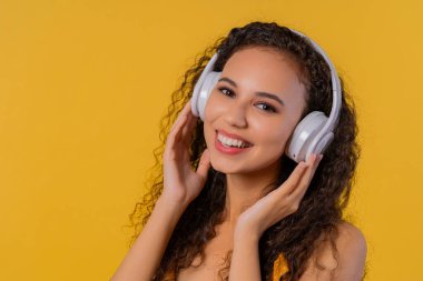 Positive woman listening music, enjoying with headphones on yellow studio background. Radio, wireless modern sound technology, online player. High quality photo