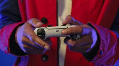 Erkek oyuncu konsolda çevrimiçi video oyunu oynuyor. Neon renkli ışığın altında kablosuz kontrolör. Adam joypad kullanarak düğmelere basıyor. Hobi, e-spor, makro görüş