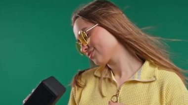 Zengin saçlarıyla dans eden, yeşil stüdyo geçmişiyle eğlenen bir kadın. Müziğin ritmine göre hareket ediyor. Young, kablosuz taşınabilir hoparlörden müzik dinliyor - modern ses sistemi