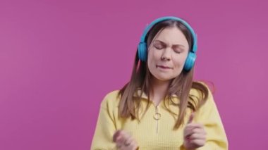 Müzik dinleyen mutlu bir kadın, pembe stüdyo arka planında kulaklıklarla dans etmekten zevk alıyor. Radyo, kablosuz modern ses teknolojisi, çevrimiçi çalar. Yüksek kalite 4k