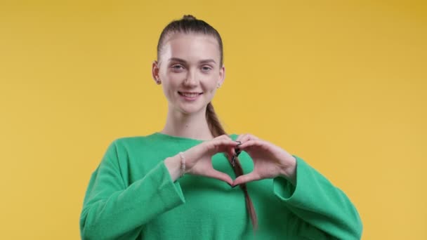 笑的漂亮女人表现出心形的迹象 有黄色背景的积极少年 妇女健康 志愿服务 慈善捐赠 感恩象征 调情概念 高质量4K — 图库视频影像