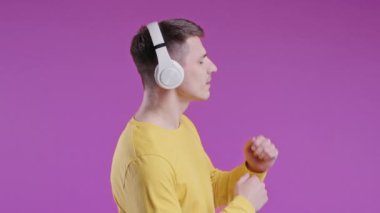 Olumlu genç adam müzik dinliyor, Violet stüdyosunun arka planında kulaklıkla dans etmekten hoşlanıyor. Radyo, kablosuz modern ses teknolojisi, çevrimiçi çalar. Yüksek kalite 4k