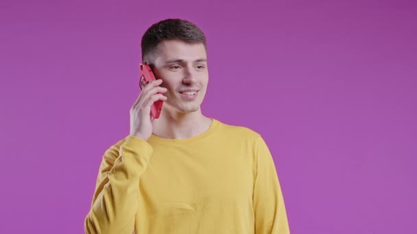 笑积极的十几岁的家伙通过电话 善意的笑话 有紫色背景的年轻人 有智能手机的电话 高质量4K — 图库视频影像