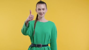 El işaretli şık bir kadın, baş parmak işareti gibi. Mutlu bayan, doğru seçim, harika bir anlaşma, sarı arka plan. Pozitif kadın model kameraya gülümser, onay, güven konsepti. kalite 4k
