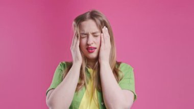 Acı çeken güzel bir kadının portresi baş ağrısı, pembe stüdyo portresi. Ellerini başının üstüne koyan bir kız. Migren sorunları, ilaç, hastalık, manyetik fırtınalar kavramı. 4k