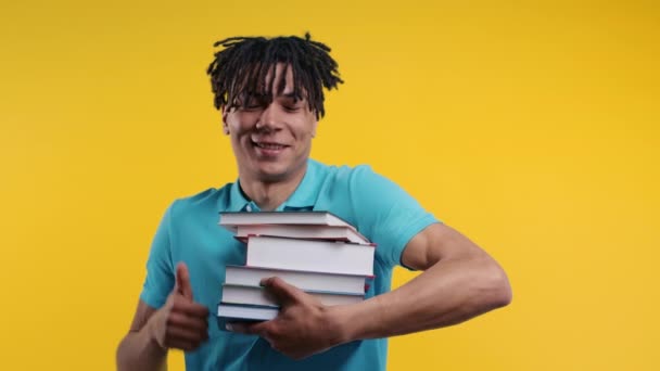 年轻的非洲裔美国人学生手里拿着一堆堆来自大学图书馆的黄色背景的书籍 快乐的家伙笑了 他很高兴毕业了 出国留学了 — 图库视频影像