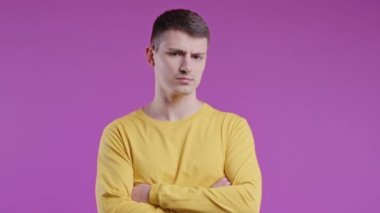 Kollarını kavuşturup birine kızgın hisseden üzgün bir genç adam. Gençlerin maksimalizmi. Yüz ifadeleri, duygular ve duygular. Vücut dili. Pembe arka planda kendine güvenen bir adam..