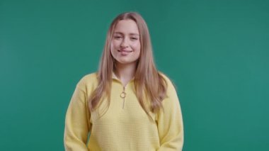 Sarı kazaklı, mütevazı ve utangaç bir kadın yeşil stüdyo arka planında kameraya bakıyor. Gülümseyen sarışın bir kadının güzel portresi. 4k