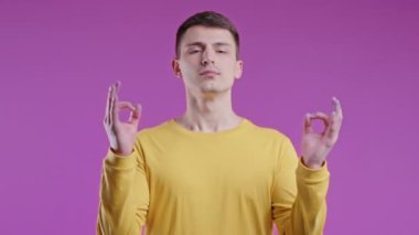 Sakin adam rahatlıyor, meditasyon yapıyor, stresi reddediyor. Kıvırcık saçlı adam derin nefes alıyor, Violet 'ın stüdyo geçmişini sakinleştiriyor. Yoga, ahlaki denge, zen konsepti. Yüksek kalite 4k