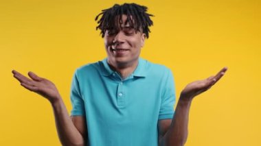 Kafası karışmış Afrikalı Amerikalı bir adam, omuzları yukarıda, yardım edemiyor, bilmiyorum jestler yapıyor. Zor soru, suçlu tepkisi, sarı arka plandaki kafası karışmış genç adam. Yüksek kalite 4k