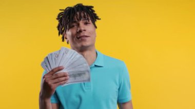 Zengin, heyecanlı, nakit parası olan Afrikalı bir adam. Sarı duvarda Amerikan Doları banknotları. İkramiyenin sembolü, kazanç, zafer, kazanan piyango. Yüksek kalite 4k