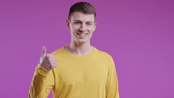 肯定的な男は 親指をジェスチャーのように手のサインをします 黄色の幸せな学生の男 正しい完璧な選択 大きな取引 ピンクのスタジオの背景 高品質4K — ストック動画