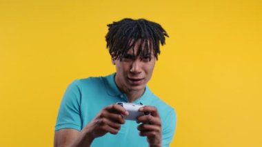 Rastalı saçlı yakışıklı Afro-Amerikan adam sarı stüdyo duvarında joystick ile TV 'de heyecan verici video oyunu oynuyor. Modern teknolojiyi kullanarak. 4k