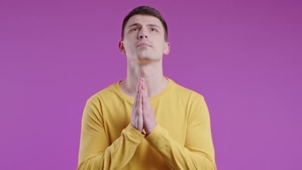 Молодой Человек Молится Руками Фиолетовом Фоне Парень Умоляет Кого Удовлетворить — стоковое видео