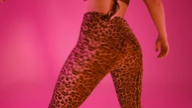 Leopar pantolonlu, modern dans eden seksi kadın. Kız sallanıyor, poposunu sallıyor stüdyo arka planına yakın çekim yapıyor, neon ışığı yanıyor. Yavaş çekim, 4k