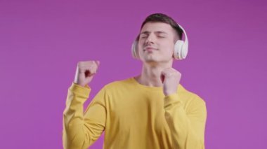 Olumlu genç adam müzik dinliyor, Violet stüdyosunun arka planında kulaklıkla dans etmekten hoşlanıyor. Radyo, kablosuz modern ses teknolojisi, çevrimiçi çalar. Yüksek kalite 4k