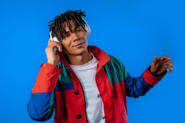 Müzik dinleyen, mavi stüdyo arka planında kulaklıklarla dans eden Afro-Amerikan genç bir adam. Radyo, kablosuz modern ses teknolojisi, çevrimiçi çalar. Yüksek kalite
