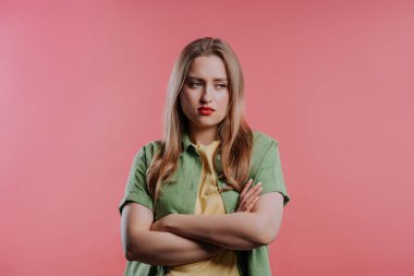 Kolları çaprazlanmış, birine kızgın genç bir kadını gücendirdim. Gençlerin maksimalizmi. Yüz ifadeleri, duygular ve duygular. Vücut dili. Pembe arka planda kendine güvenen bir bayan..