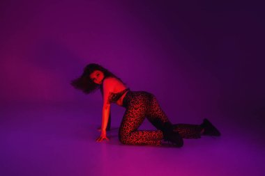 Seksi kadın esnek hareketler sergiliyor, vücudunu sallıyor. Neon Stüdyoda baştan çıkarıcı ateşli dans. Dar elbiseli ve spor ayakkabılı bayan dansçı..