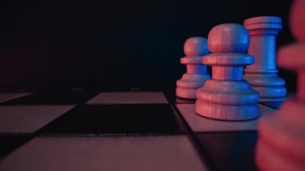 パーティーの競争の前に木製のチェス盤のスライダーマクロショット チェスの駒 ボード戦略ゲーム チームワーク成功ビジネスインテリジェンススポーツの概念 カラフルなネオンライト — ストック動画