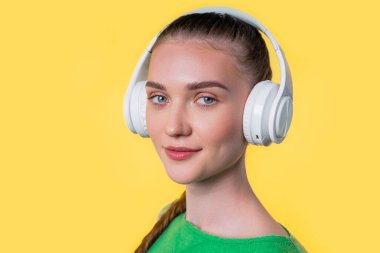 Müzik dinleyen pozitif bir kadın, sarı stüdyo arka planında kulaklıklarla eğleniyor. Radyo, kablosuz modern ses teknolojisi, çevrimiçi çalar. Yüksek kalite