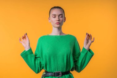 Sakin bir kadın dinleniyor, meditasyon yapıyor, stresi reddediyor. Sarışın kadın derin nefes alıyor, sarı stüdyo arka planını sakinleştiriyor. Yoga, ahlaki denge, zen konsepti. Yüksek kalite