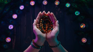 Mantraları ya da duaları okuyan kadın meditasyonlar sırasında kullanılan tahta boncukları sayıyor. Bayan mumların ve tavus kuşu tüylerinin arasında oturuyor. Maneviyat, din, Tanrı kavramı..