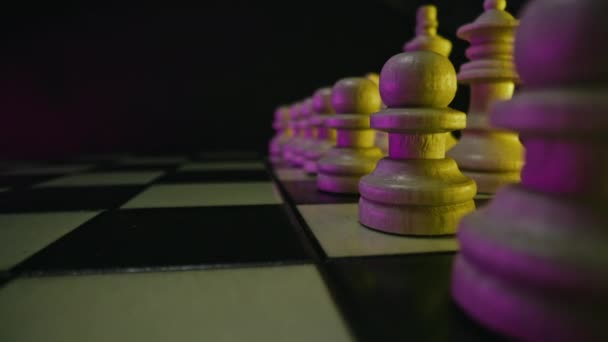 パーティーの競争の前に木製のチェス盤のスライダーマクロショット チェスの駒 ボード戦略ゲーム チームワーク成功ビジネスインテリジェンススポーツの概念 カラフルなネオンライト — ストック動画