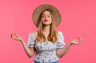 Sakin bir kadın dinleniyor, meditasyon yapıyor, stresi reddediyor. Sarışın kadın derin nefes alıyor, pembe stüdyo arka planını sakinleştiriyor. Yoga, mandala, ahlaki denge, zen konsepti. Yüksek kalite