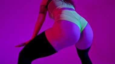 Dans eden seksi kadın modern dans - twerk. Kız sallanıyor, poposunu sallıyor stüdyo arka planında, neon ışıkları altında. Yavaş çekim, 4k
