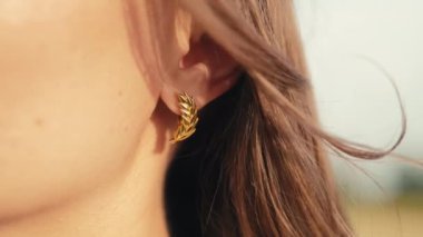 Buğday tarlasında poz veren altın buğday rengi küpeli güzel bir kadın. Mücevher detaylarını kapat. Yüksek kalite 4k görüntü