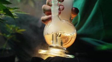 Tıbbi marihuana içen bir adam, evdeki neon ışıkta cam su bongu. Esrar tütünü, Shisha. Yüksek kalite 4k görüntü