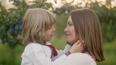 Annesiyle sevgi dolu oğlunun elma bahçesinde güneşli bir sahne. Güzel bir aile. Annesiyle birlikte 4 yaşında tatlı bir çocuk. Ebeveynlik, çocukluk, mutluluk, çocukların refahı kavramı.