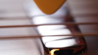 Elektro gitar telleri titreşiyor. Müzik enstrümanında arabulucuyla çalmak. Ses dalgaları, tıngırdayan akorlar, akustik ses rezonansı. Süper makro görüntüler. Yüksek kalite 4k görüntü