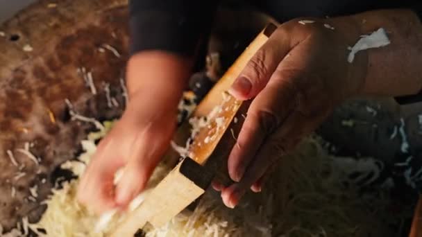 女性はキャベツをグレーターでこすり 伝統的なウクライナの発酵サラダを細断されたニンジンから調理します 古代の木造トラフでチョップした野菜を混ぜます 高品質の4K映像 — ストック動画