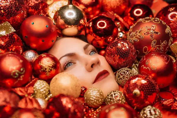Young pretty woman face lights up with joy in Christmas tree toys balls. Wonder, happiness mood. Touch of magic. Holiday-themed projects, family-focused content or sentimental storytelling.