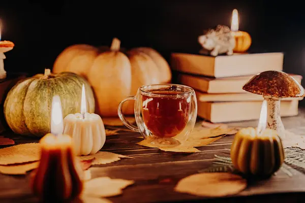 Glass cup of tea among pumpkin candles. Autumn-themed content, cafe promotions or visual storytelling that exudes comfort. Touch of intimacy, tranquil and inviting atmosphere.