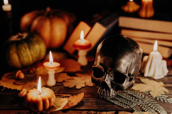 Mystique background - bronze human skull with candles. Visual gothic aesthetic. Autumn pumpkin candle, falling leaves. Ambience of fall. Seasonal promotions or dramatic visual storytelling.
