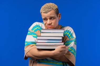 Lazy man student is dissatisfied with amount of books, homework in high school, blue background. Guy in displeasure, he is annoyed, discouraged frustrated by studies. High quality photo