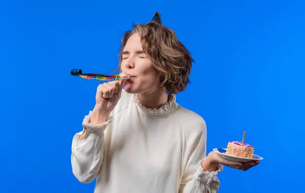 Happy birthday woman making wish - candle on cake. Girl smiling, celebrating anniversary. Young stylish lady on blue background. High quality photo