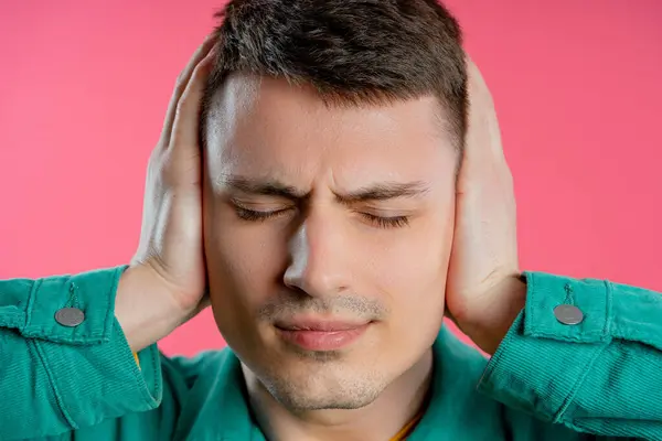 Annoyed young man with shut ears on pink background. Guy block annoying sounds, music, shouts or noise. Rolling eyes. Concept of conflict, problems. High quality