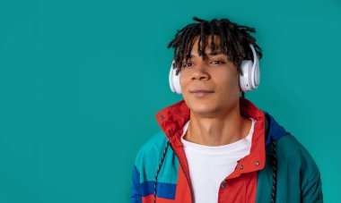 Müzik dinleyen, mavi stüdyo arka planında kulaklıklarla dans eden Afro-Amerikan genç bir adam. Radyo, kablosuz modern ses teknolojisi, çevrimiçi çalar. Yüksek kalite. 