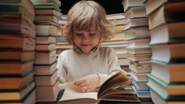 Yakışıklı küçük çocuk kütüphanede kitap sayfalarını karıştırıyor. İlkokul çocuğu kitapçıda ya da kitapçıda okumayı seviyor. Yüksek kalite 4k görüntü