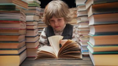Düşünceli anaokulu yakışıklısı çocuk kütüphanede kitap sayfalarını çeviriyor. Küçük çocuk okumayı seviyor. Kendini eğitme, bilim, bilgelik konsepti. Yüksek kalite 4k görüntü