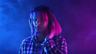 Mutlu kadın kafayı bulur, müzik dinler, koyu renkli neon ışıklı stüdyo arka planında kulaklıklarla dans etmekten zevk alır. Radyo, kablosuz modern ses teknolojisi, çevrimiçi çalar. Yüksek kalite 4k