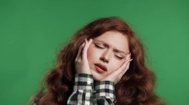Acı çeken güzel bir kadının portresi baş ağrısı, yeşil stüdyo portresi. Güzel bayan ellerini başının üstüne koyuyor. Migren sorunları, ilaç, hastalık, manyetik fırtınalar kavramı. 4k