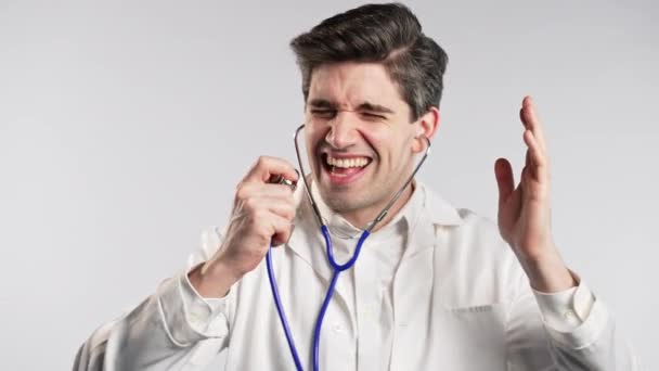 微笑的医生跳舞有趣 对听诊器唱歌 工作上的成功和好运 穿着专业医用白衣的英俊医生在工作室背景下被隔离 高质量的4K镜头 — 图库视频影像