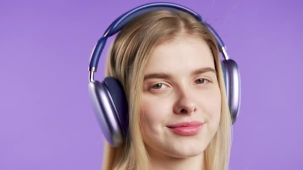 ハッピーな女性はハイになり 音楽を聴き バイオレットスタジオの背景にヘッドフォンでダンスを楽しんでいます ラジオ ワイヤレス現代サウンド技術 オンラインプレーヤー 高品質4Kについて — ストック動画