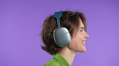 Mutlu kadın kafayı buluyor, müzik dinliyor, Violet stüdyosunun arka planında kulaklıklarla dans ediyor. Radyo, kablosuz modern ses teknolojisi, çevrimiçi çalar. Yüksek kalite 4k