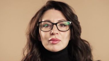 Gülümseyen olgun bir iş kadını ya da dudak tutan bir öğrenci, bej renkli stüdyo arka planı. Şşş, sır, sessizlik, komplo, dedikodu konsepti olan hoş bir bayan. Yüksek kalite 4k